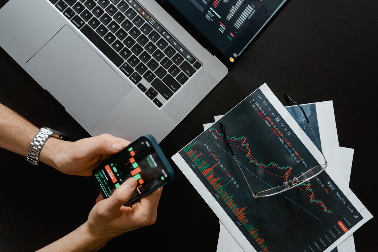 The Art of Drawing Readers In: Your attractive post title goes here Hands using smartphone beside laptop with stock charts, showcasing digital trading.